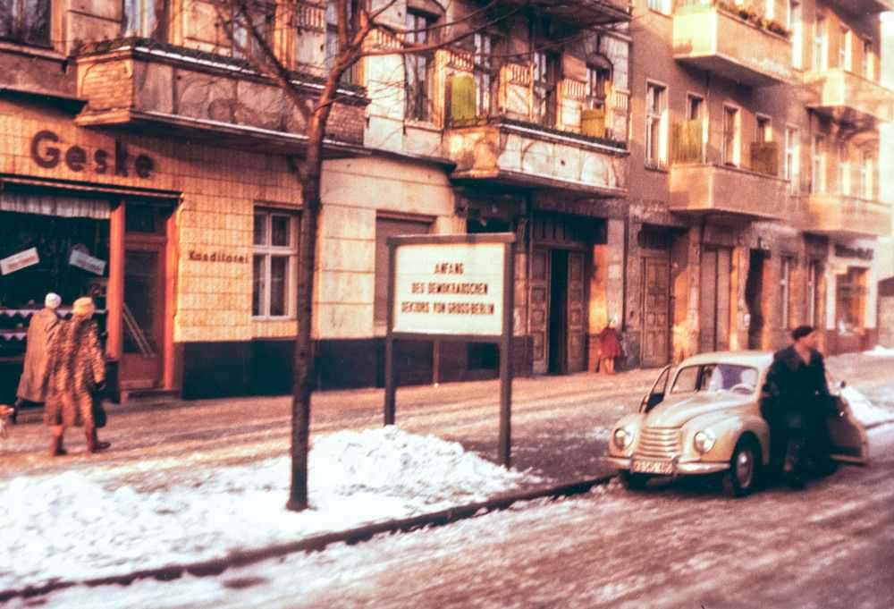 A snowy Berlin street scene in the winter of 1956. Translated, the sign reads 'Start of the Democratic Sector of Greater Berlin', marking the boundary of the Soviet sector.
