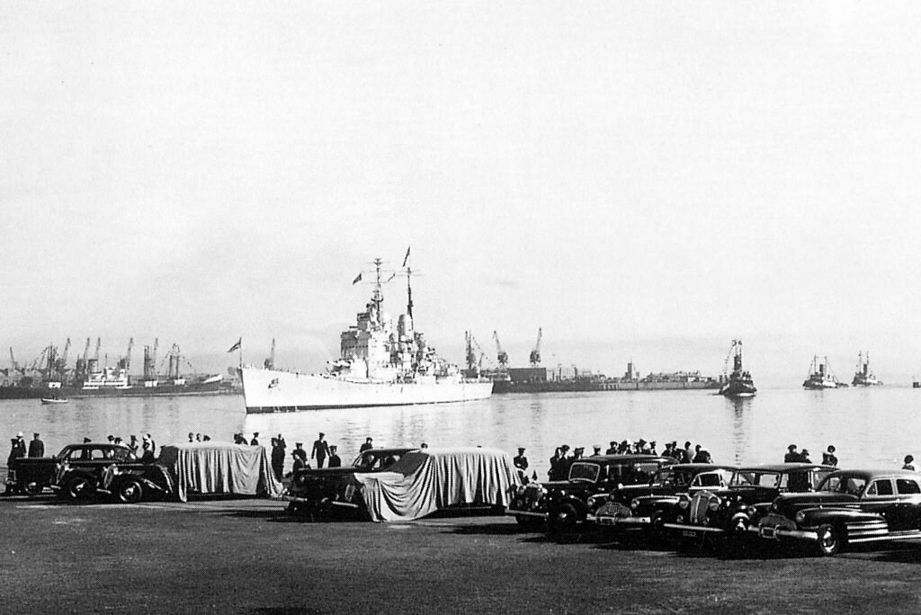 Officials waiting for the battleship HMS Vanguard (carrying the Royal Family) to dock on the 17th February 1947 The two Daimlers to be used by the Royals is covered to keep them cool in the February heat.