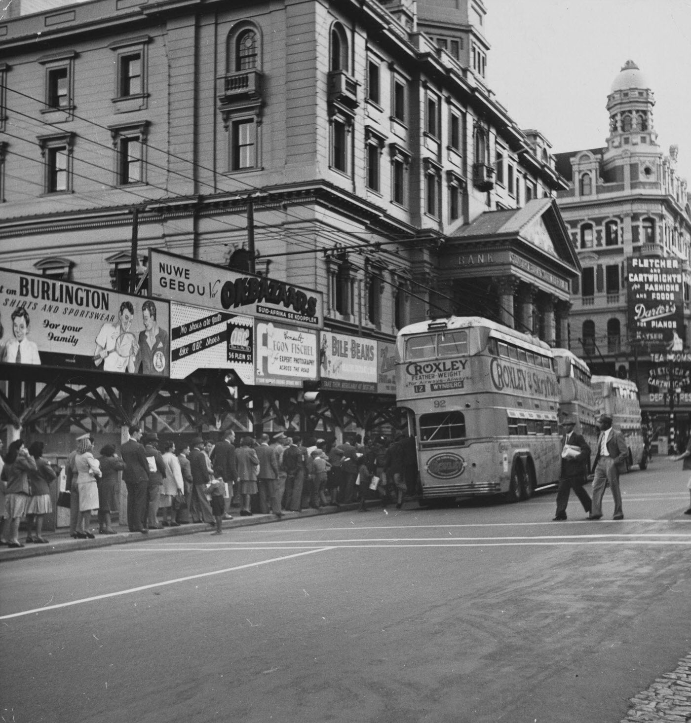 People slowly file onto a double-decker bus parked outside a bank, in Adderley Street.
