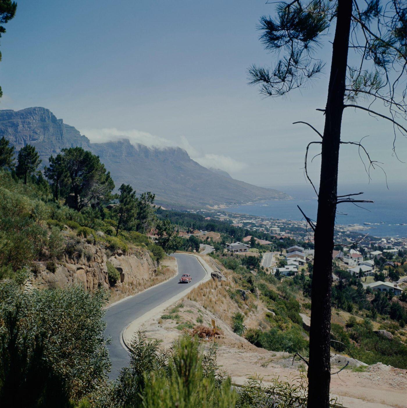 A car drives along a road above Camps Bay, a suburb of Cape Town overlooking the Atlantic Ocean, 1966