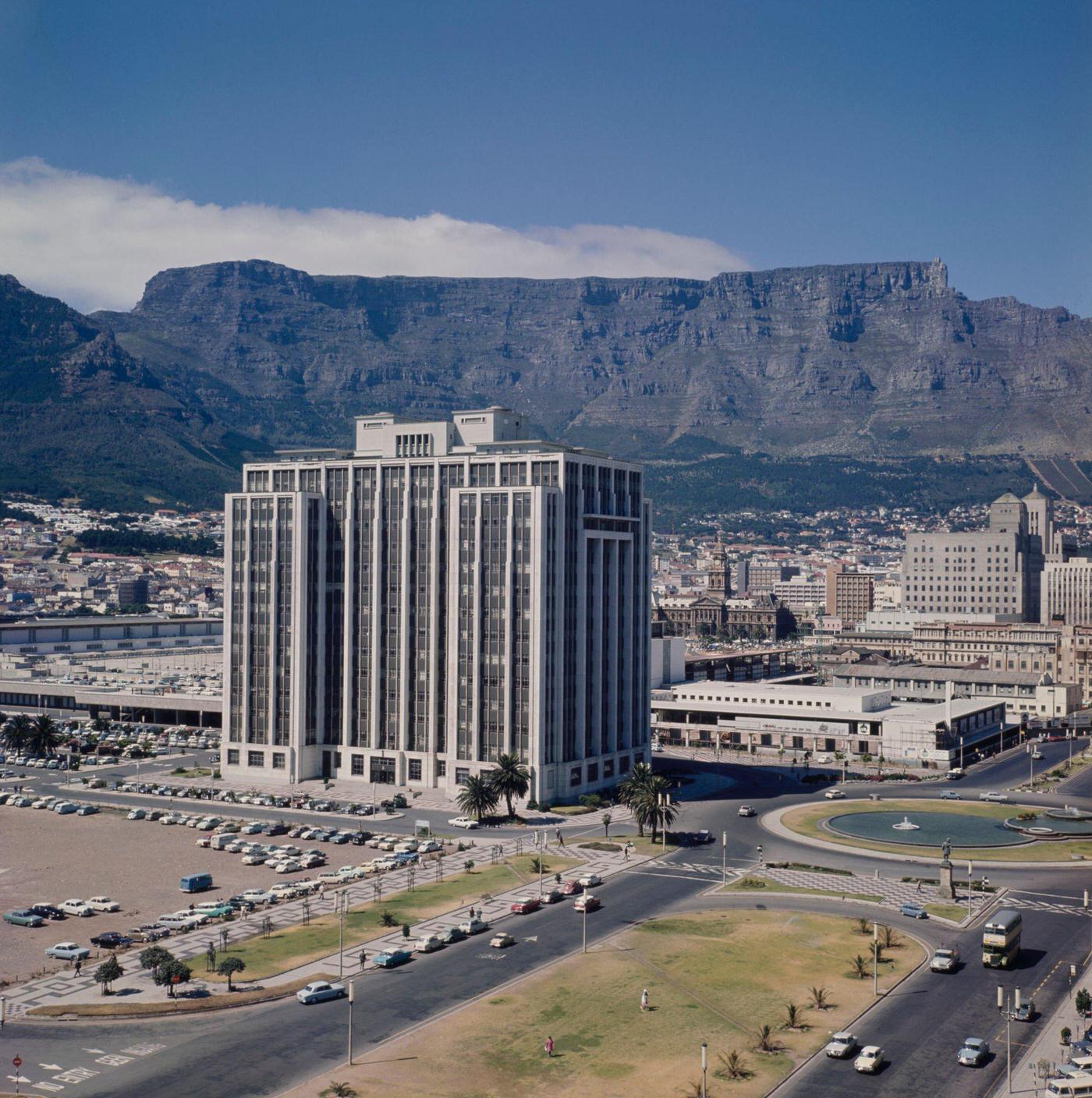 Traffic drives past the Adderley Street Fountain and down Heerengracht Street in the Foreshore Place district of the city of Cape Town, 1960