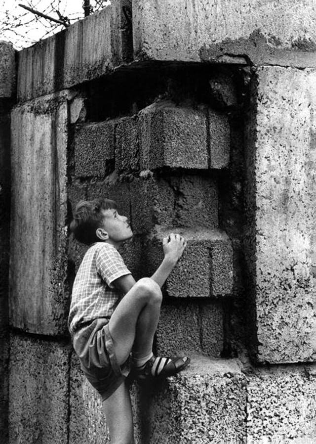 A young boy, on the West Berlin side, climbing the Berlin Wall between East and West Berlin.