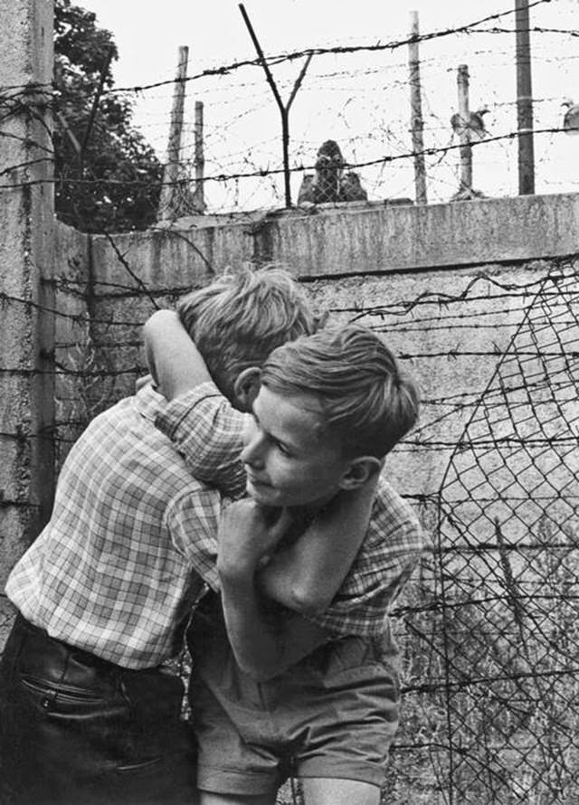Boys wrestling on western side of the Berlin Wall near Bernauer Strasse while East German border guard watches with binoculars.