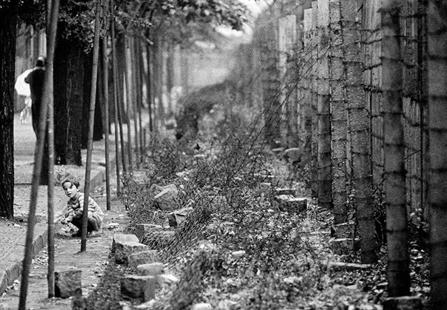 A young girl playing near a barbed wire fence along the border Wall between East and West Berlin.