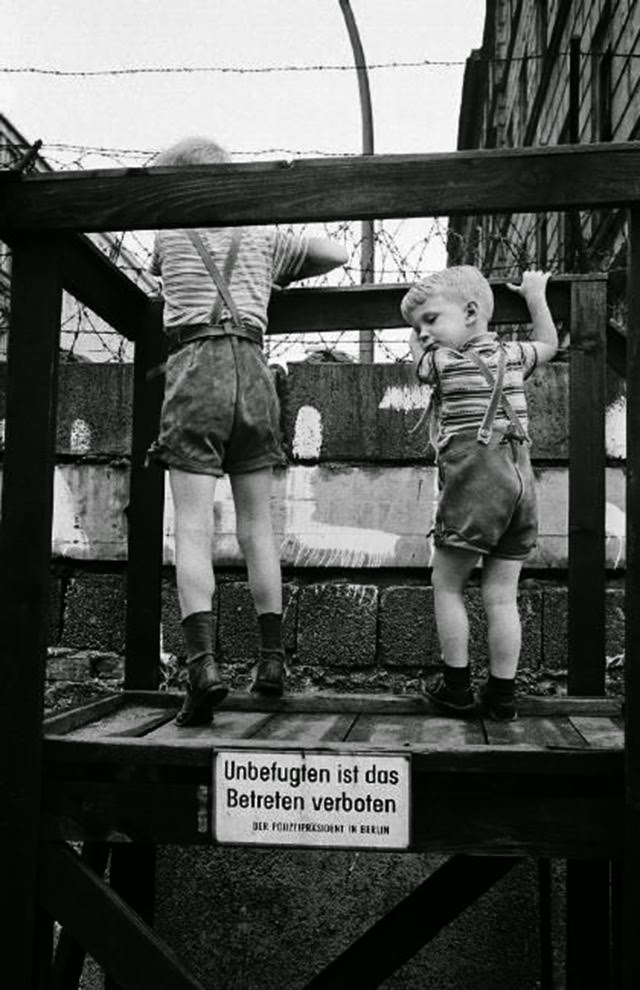 Two boys in leather shorts standing on a viewing platform at the western side of the Berlin Wall.