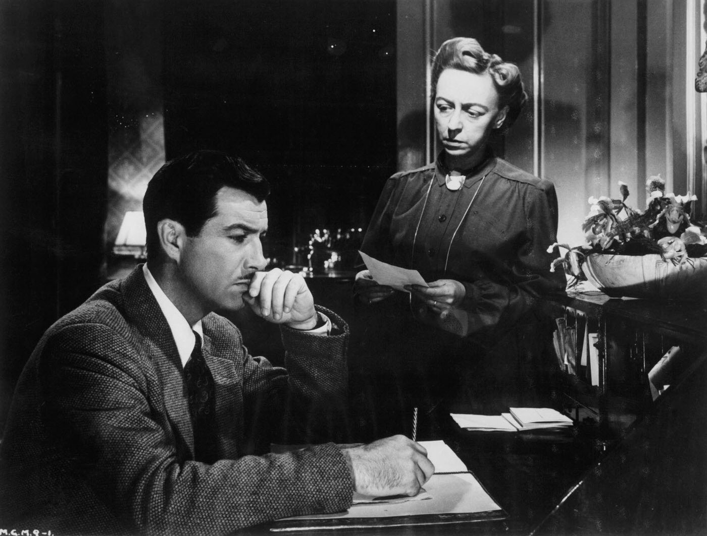Robert Taylor writing as an unidentified woman looks at him in a scene from the film 'Conspirator', 1949.