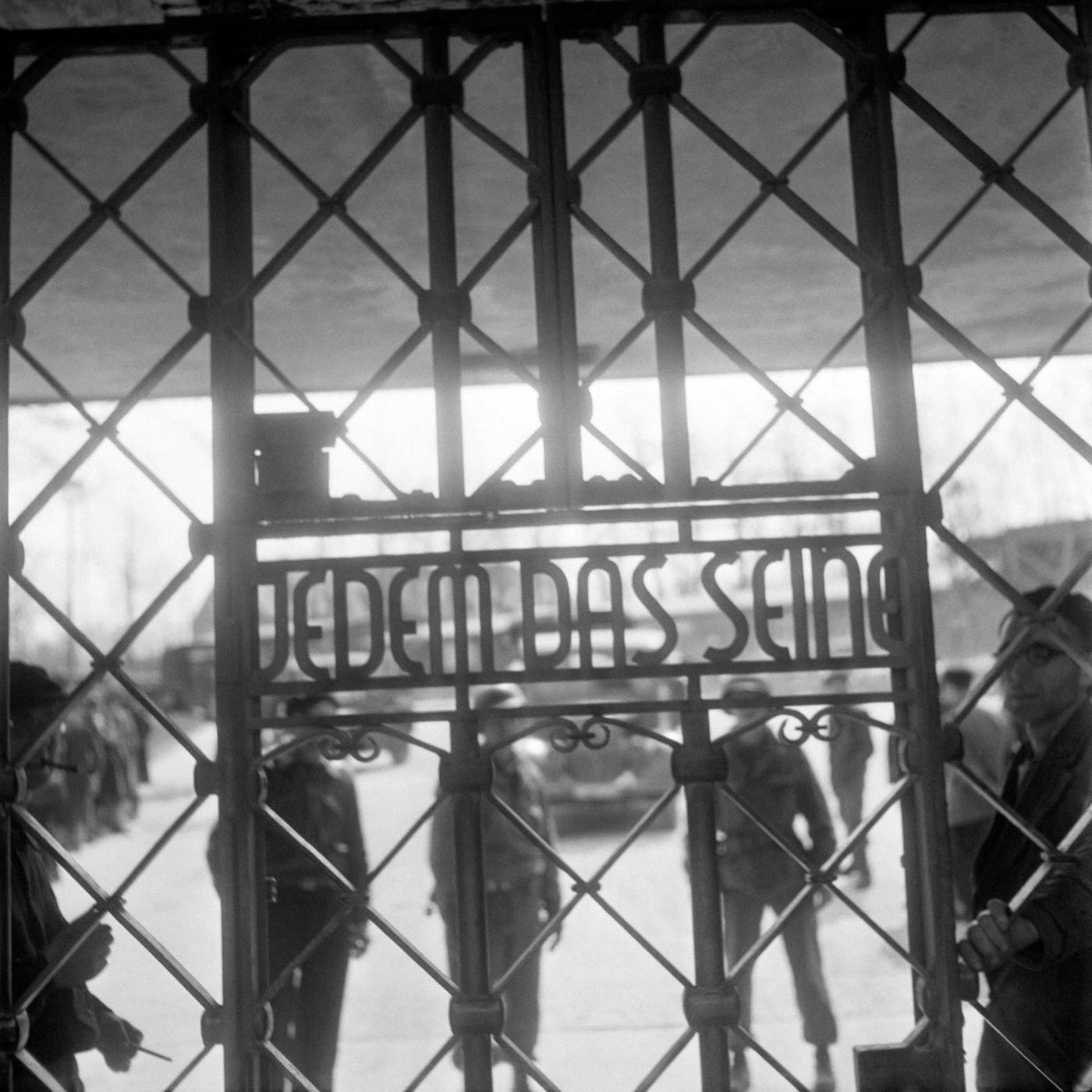 Prisoners and US army soldiers stand behind the gate of Buchenwald concentration camp with the inscription "Jedem das seine" (to each his own), April 1945.