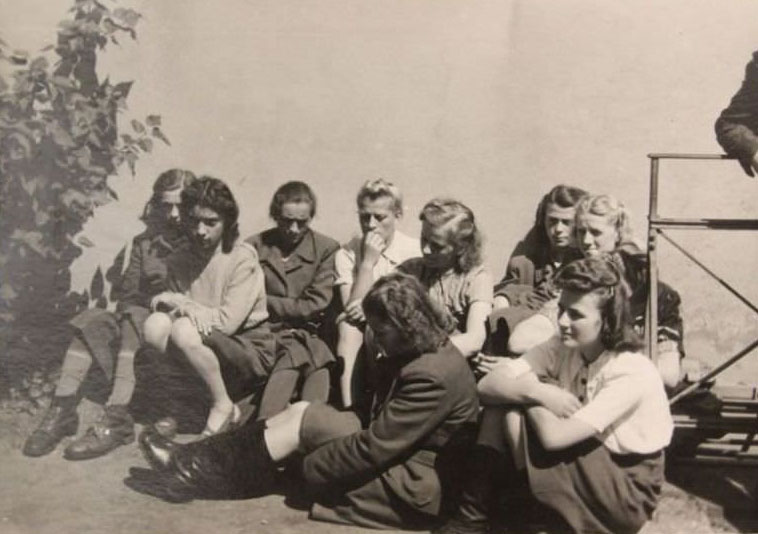 A group of young women sit outside the jail where 45 people faced charges for war crimes in 1945.