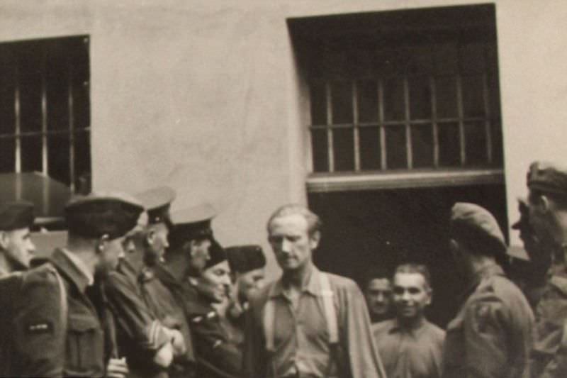A group of men are marched out of the jail cells before two rows of Allied soldiers acting as prison guards.