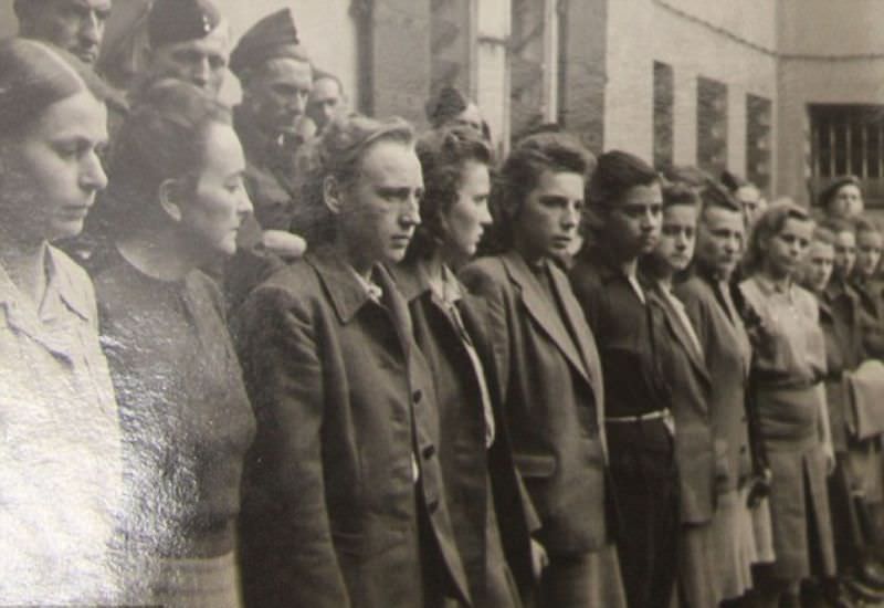 More than a dozen women, suspected of being complicit in war crimes, are displayed before a gathered crowd.