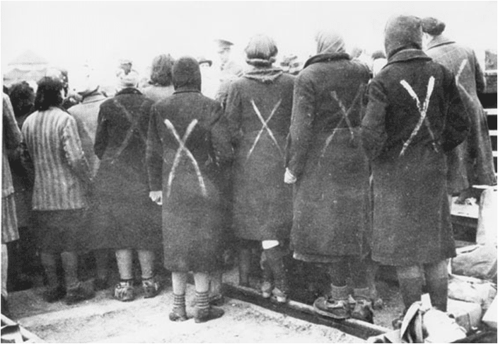 Surviving female prisoners gathered when the Red Cross arrive at Ravensbrück in April 1945. The white paint camp crosses show they are prisoners, not civilians.