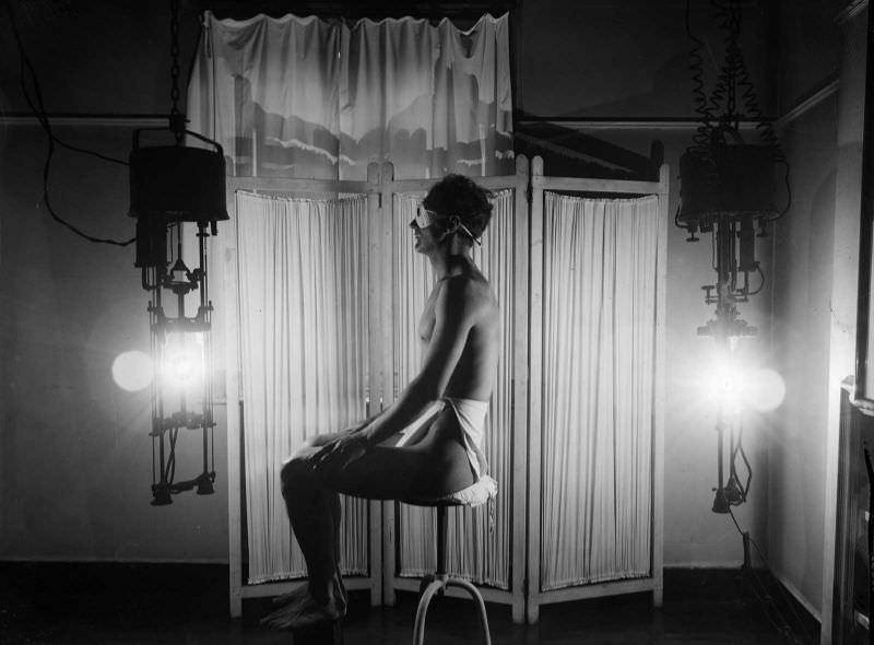 Wearing only a towel and dark goggles a man enjoys the benefits of a sun-ray lamp, circa 1930.