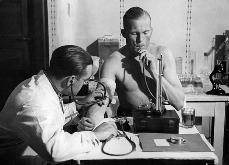 Lieutenant Radtke presses air into his lungs at a constant height with a mercury column, while the doctor checks his blood pressure, circa 1932.