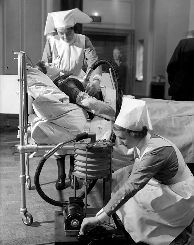 Nurses practice operating a respiratory jacket that performs a similar function to an iron lung, circa 1938.