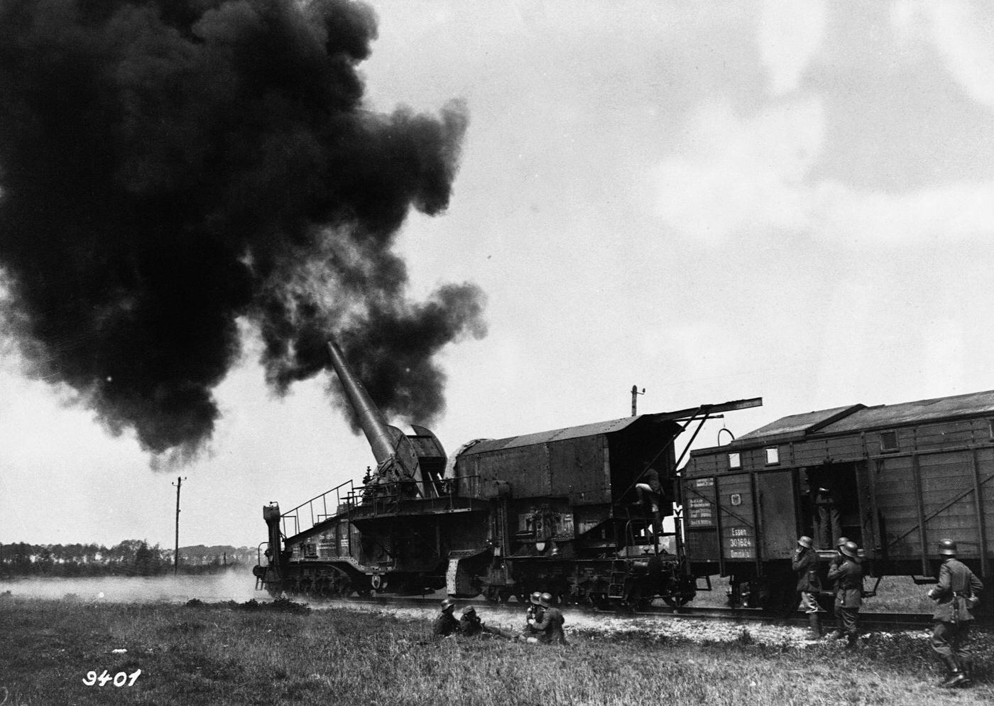 Large German artillery gun mounted on a railroad car firing a shell.