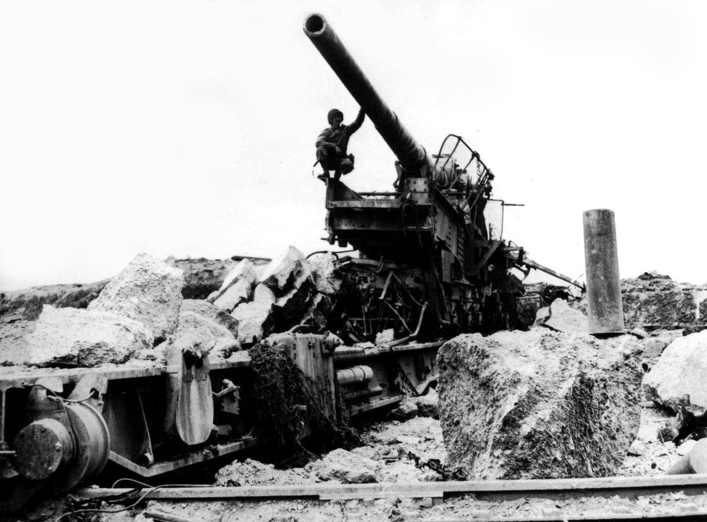An American soldier examining a giant 10-inch German railroad gun mounted on a circular track in the Cherbourg Peninsula, France.