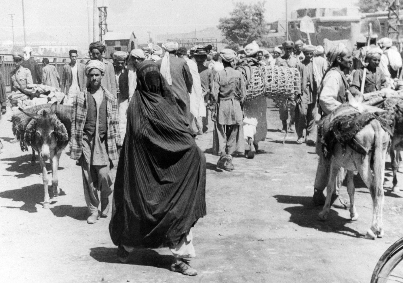 Woman in a full "burkah" on a street full of men, circa 1950s.