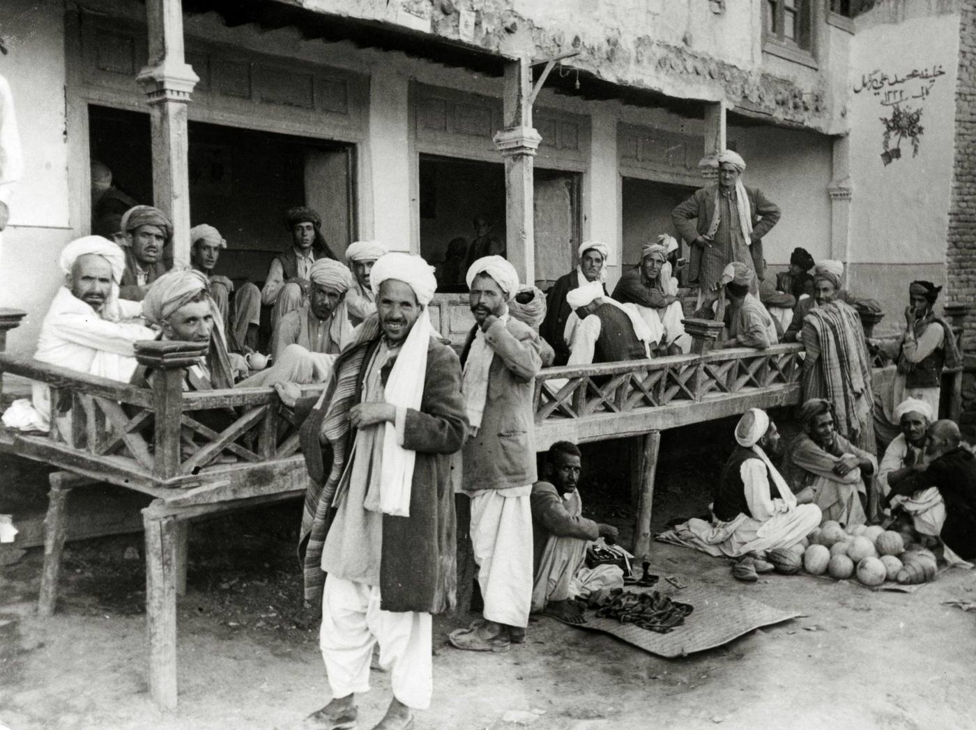 Kabul street scene with guests passing the time on a verandah, circa 1950.