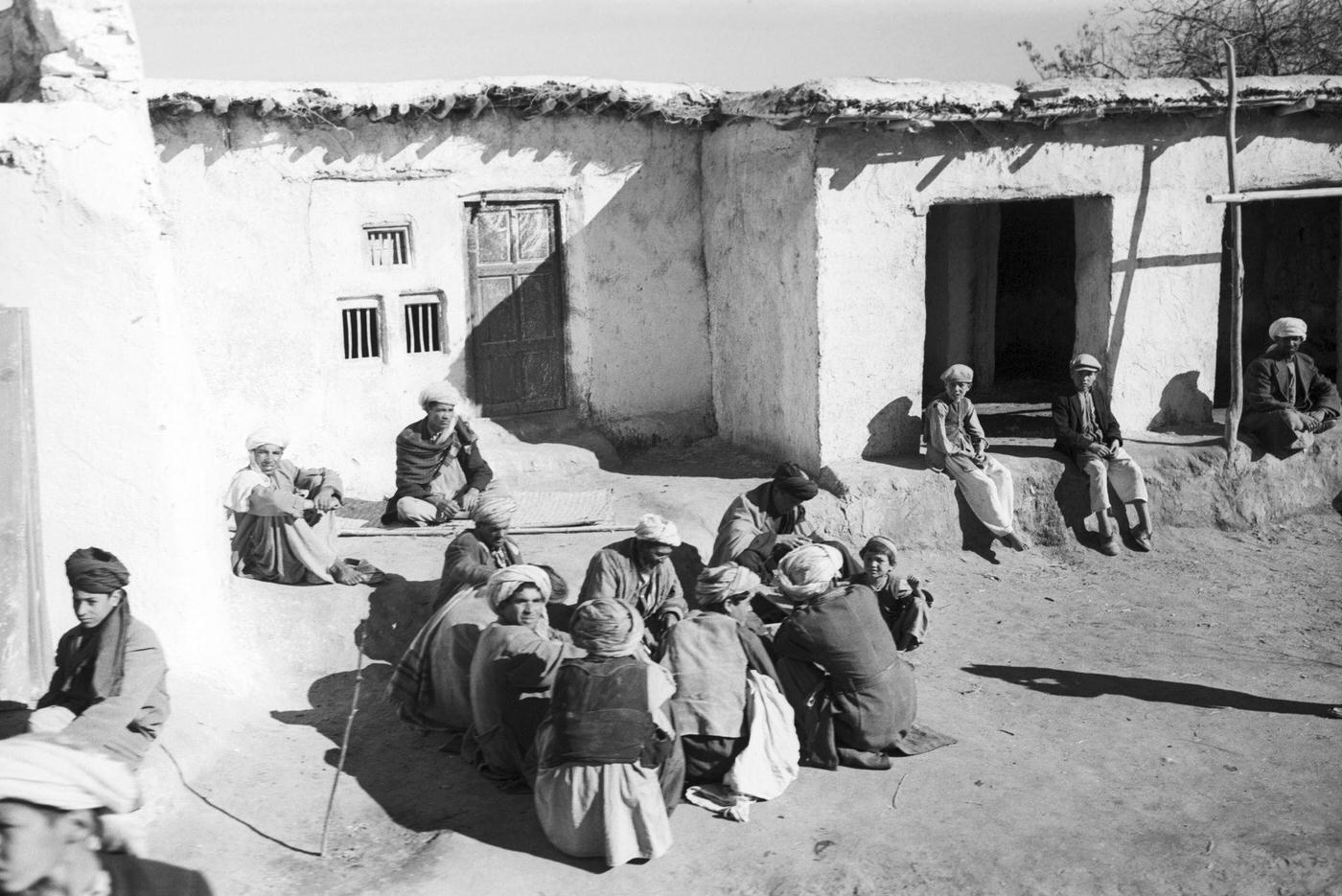 People seated on the ground in front of their house on the road to Kabul, 1959