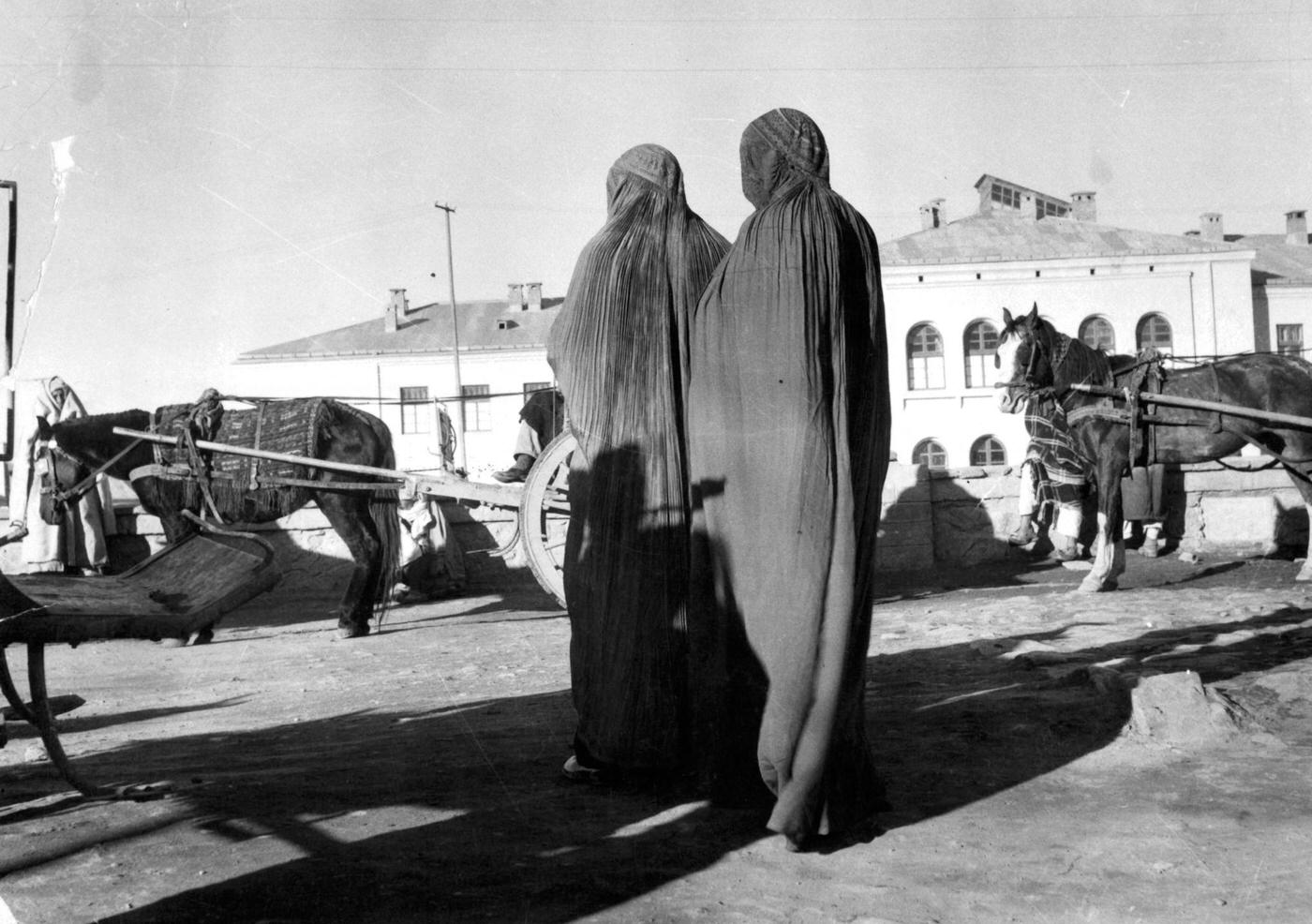 Women in veils waiting for a "taxi" ponycart in a Kabul street, 1955.