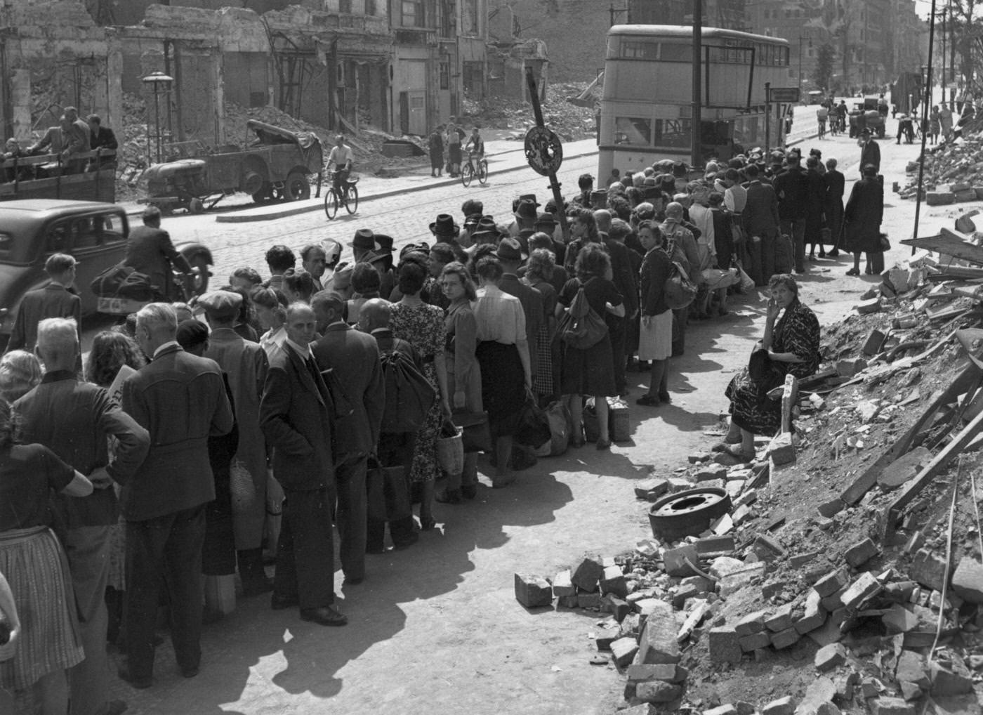 Bus queue in Berlin stands beside a pile of rubble at the end of World War II in Europe, 1945.