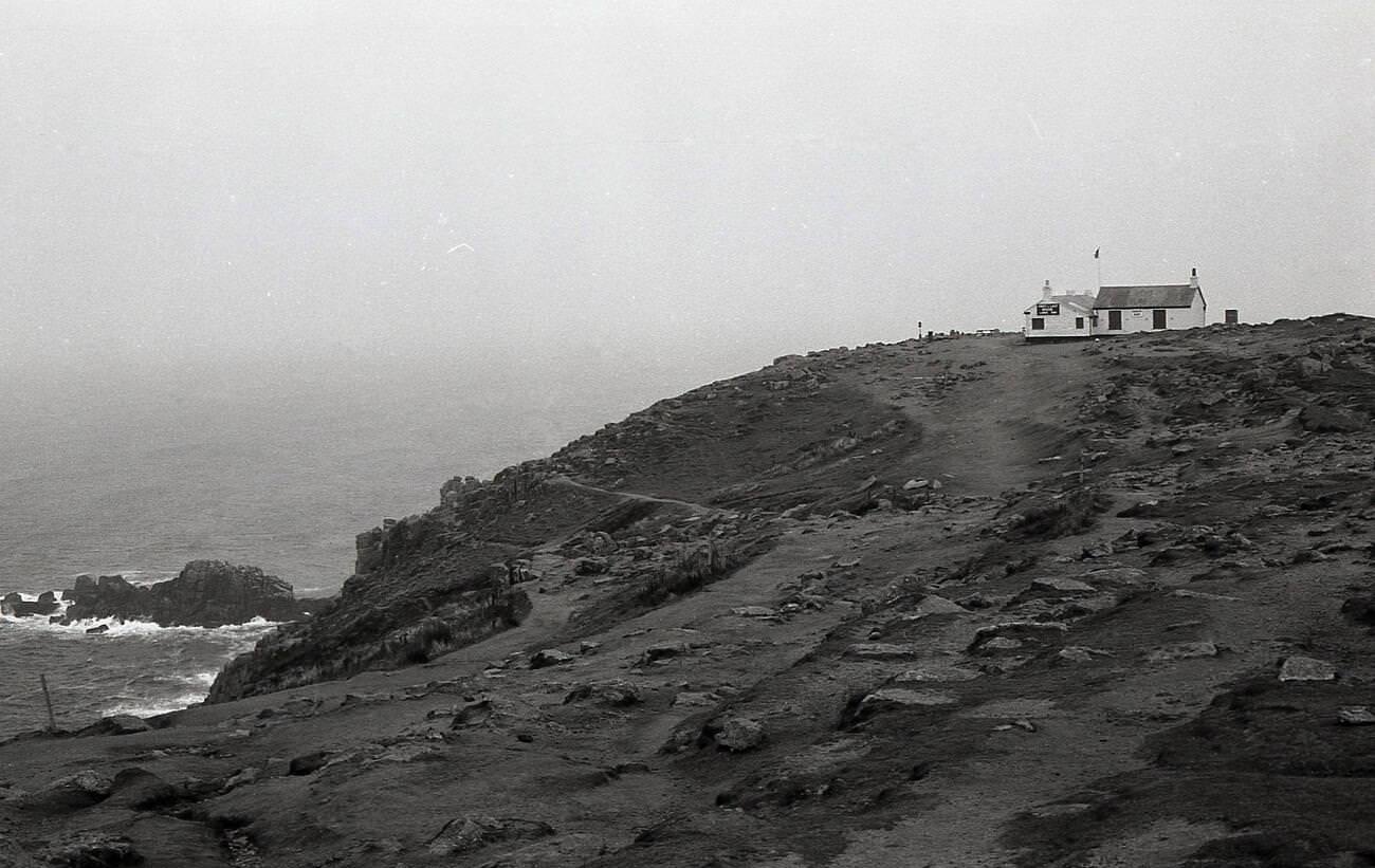 Rugged coastline at Land's End, Cornwall, with the famous tea room, the 'First & Last House' perched on the clifftop, 1970s.
