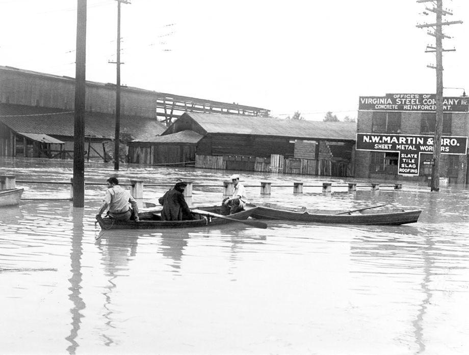 Three men used small rowboats to navigate over a submerged bridge at 17th and Dock streets in Richmond, 1935.