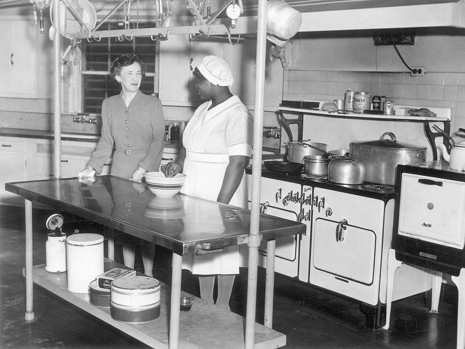 Mrs. Price looks on while Lucille, the mansion's cook, mixes up something special in the kitchen, which has been completely renovated during the Price administration, 1942.
