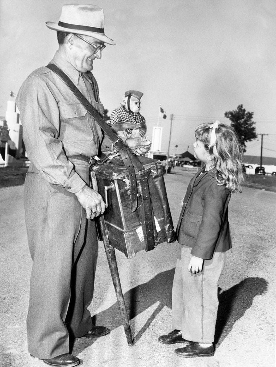 An organ grinder and his monkey entertained a young girl at the State Fair, held at the Atlantic Rural Exposition fairgrounds, 1949.