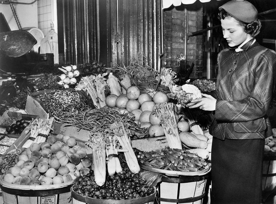 Beverly Horsley, a Miller & Rhoads fashion model, choose vegetables from a lavish display at the Sixth Street Market as part of Style Marches On, a weeklong celebration of new fall fashion in the downtown Richmond retail district, 1948.