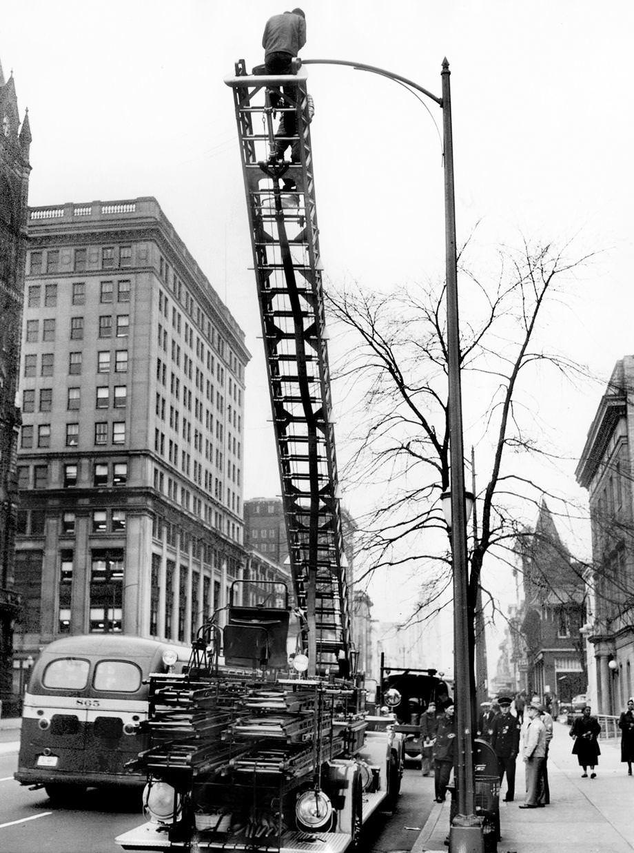 Richmond Department of Utilities workers used a 65-foot hook-and-ladder fire truck to install new lights on Broad Street after attempts to secure other ladder facilities from private companies had failed, 1953.