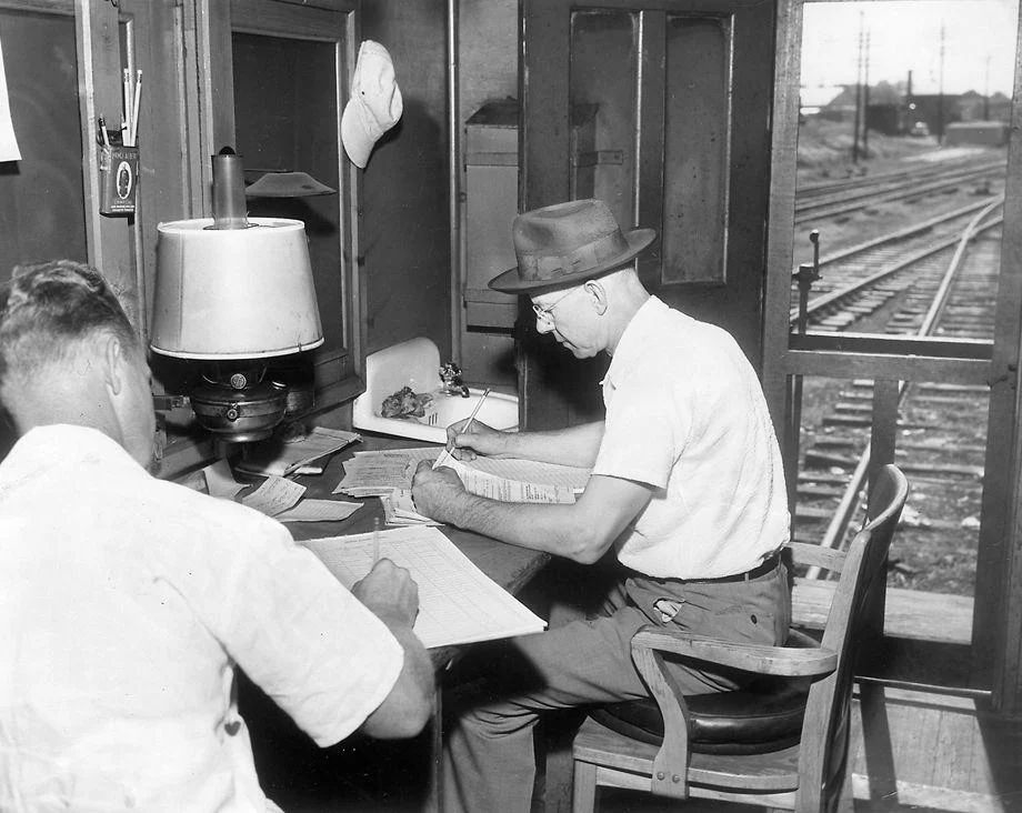 Fredericksburg and Potomac Railroad conductor H.C. Rollins (right) and flagman C.H. Smith did pre-trip paperwork in a train caboose before a ride to Washington, 1953.