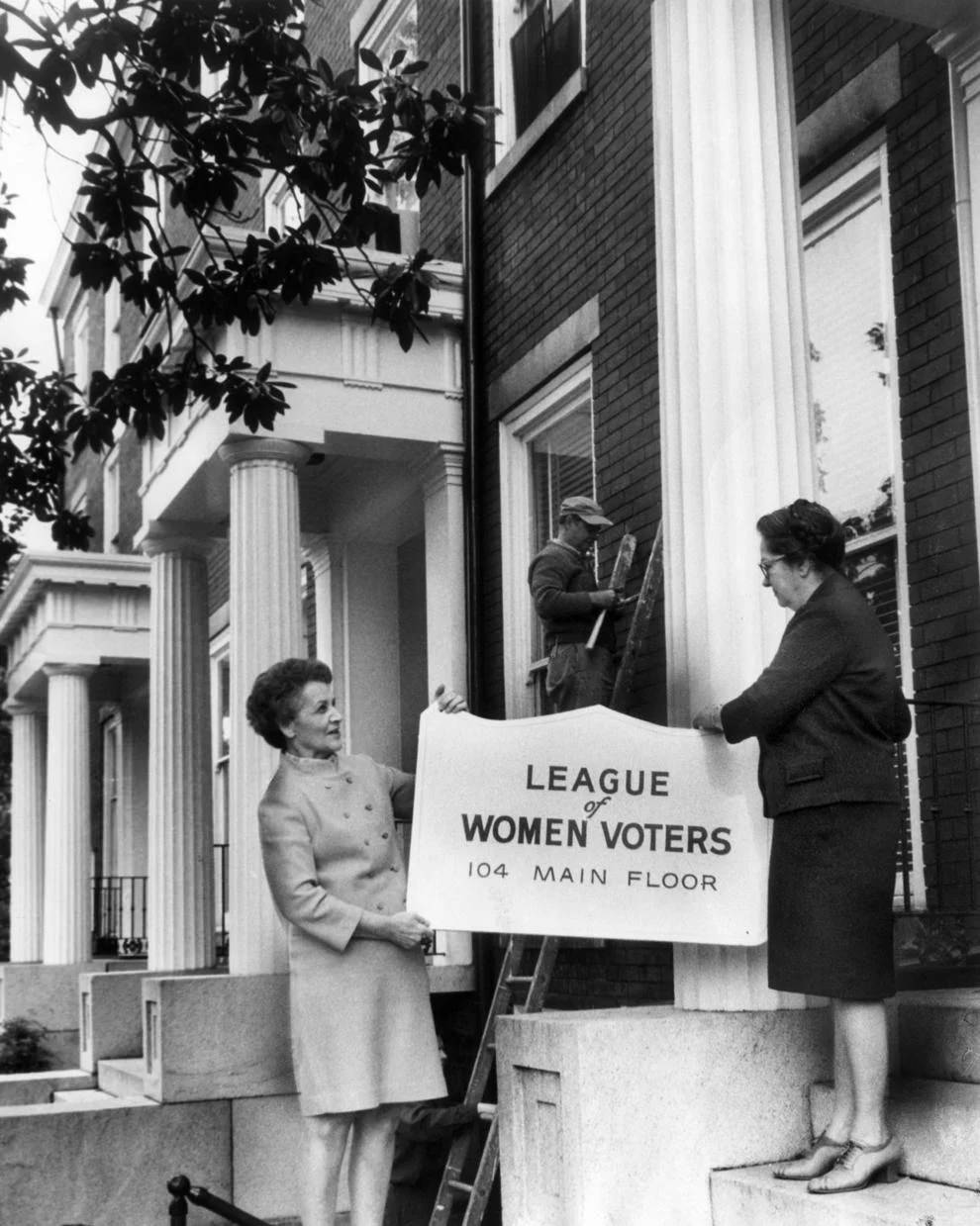 Mrs. W.H. Crockford (left) and Mrs. J.K. Higdon hung the sign outside the new state-local League of Women Voters headquarters at Linden Row in downtown Richmond, 1964.
