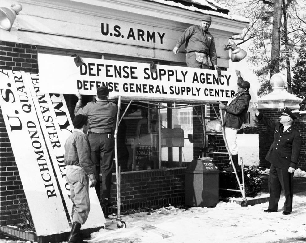 Maj. Walter Weissner (right), post engineer at the quartermaster depot at Bellwood, directs installation of a new sign pointing up the consolidation of the Military General Supply Agency and the Richmond Quartermaster Depot, effective with the new year, 1962.