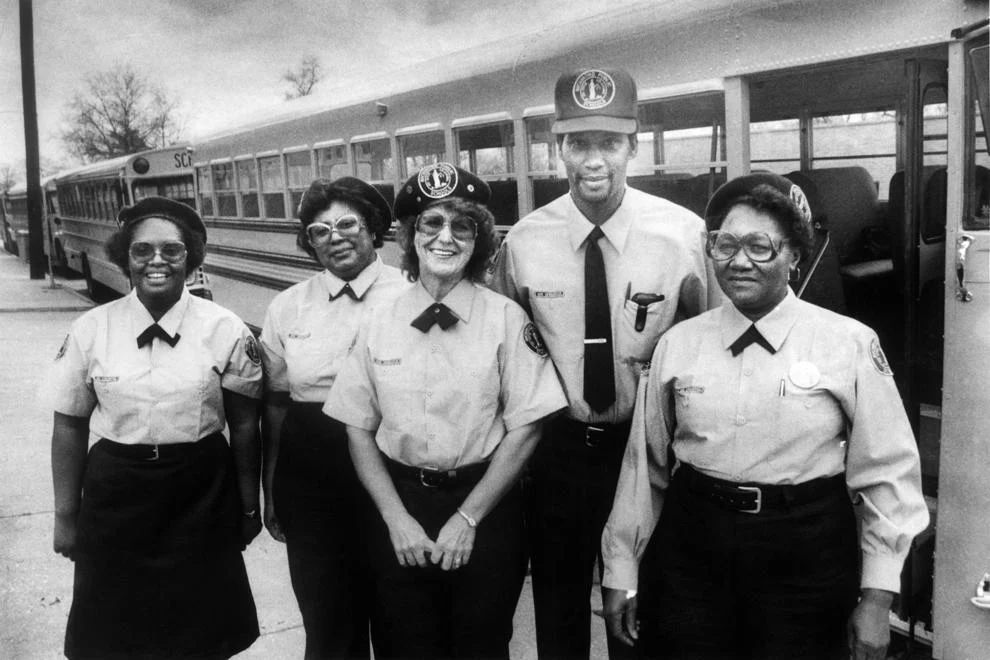 A group of Richmond school bus drivers modeled new uniforms, which included light blue shirts, navy slacks or skirts, berets or caps, and jackets and ties, 1982