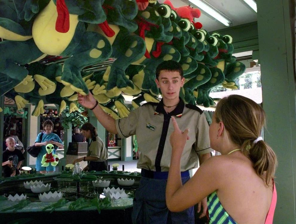 Tomas Stanek, of the Czech Republic, shows a customer at Busch Gardens what she could win if she hammers a frog into a lily Thursday, June 18, 1998.