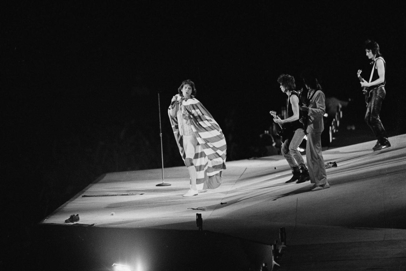 Mick Jagger, draped in an American flag, performs with Keith Richards, Bill Wyman, and Ronnie Wood , 1975.