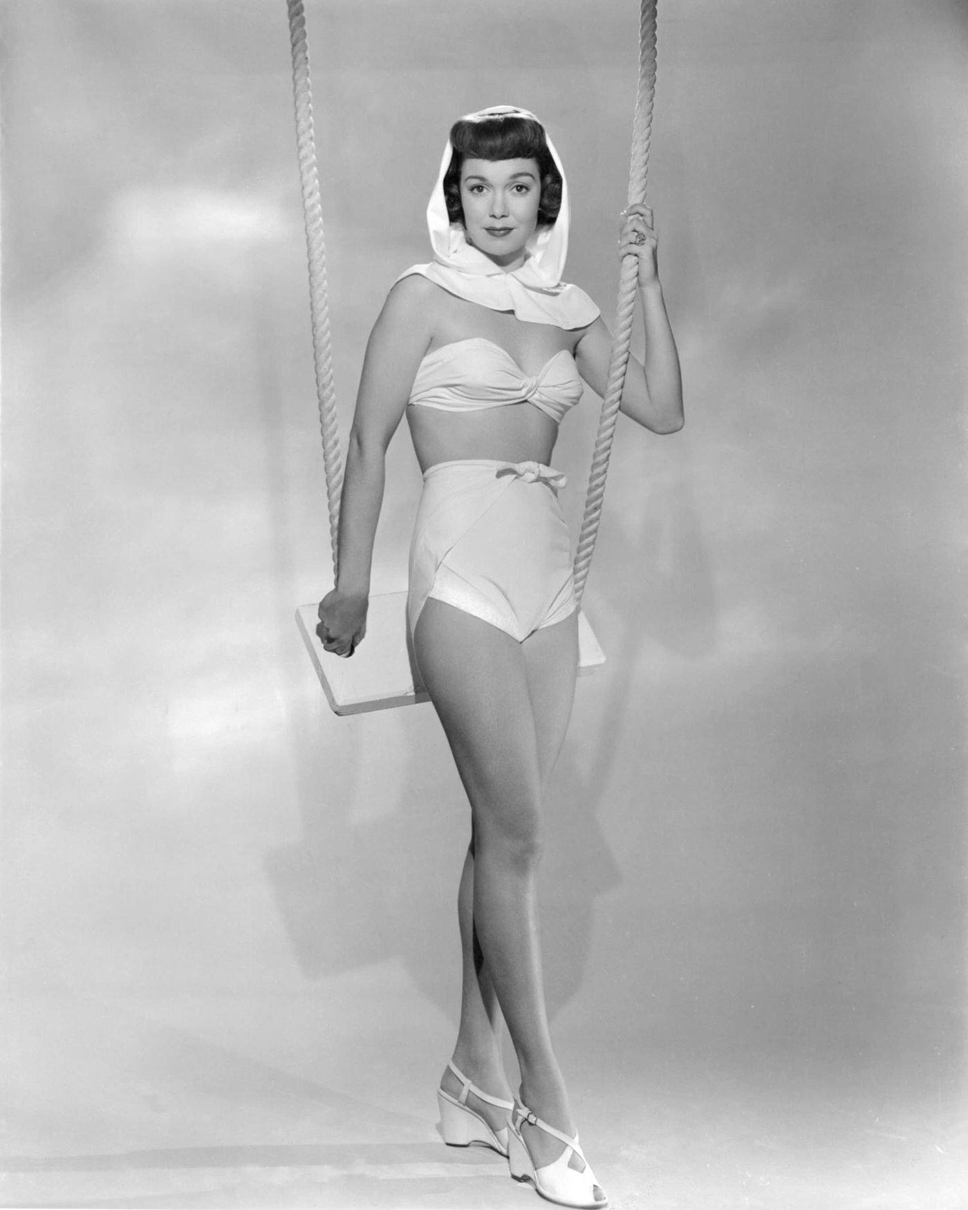 Jane Wyman, American actress and singer, leaning on a swing in a white two-piece swimsuit, 1945.