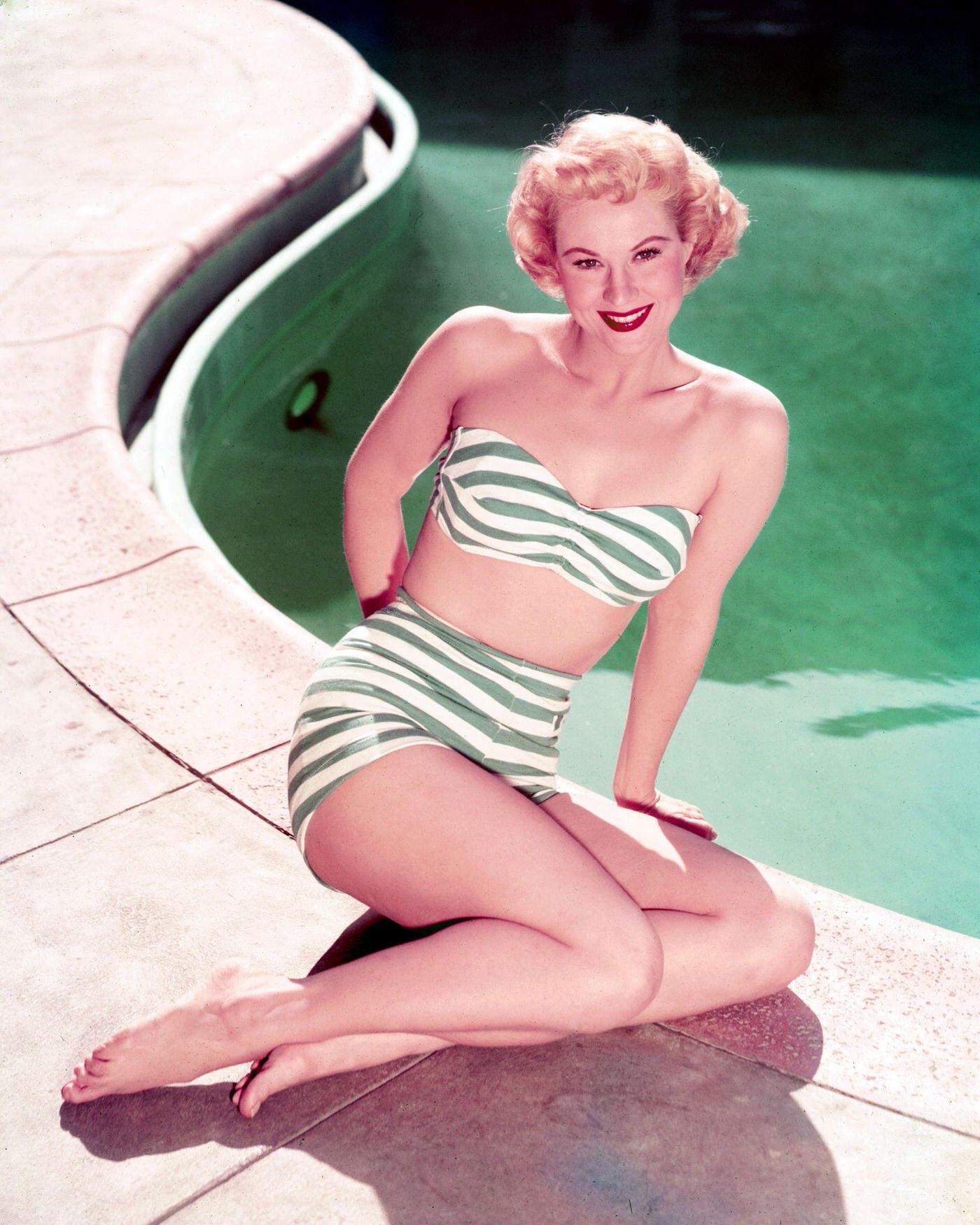 Virginia Mayo in a green-and-white striped bikini, posing at the edge of a swimming pool, 1945.