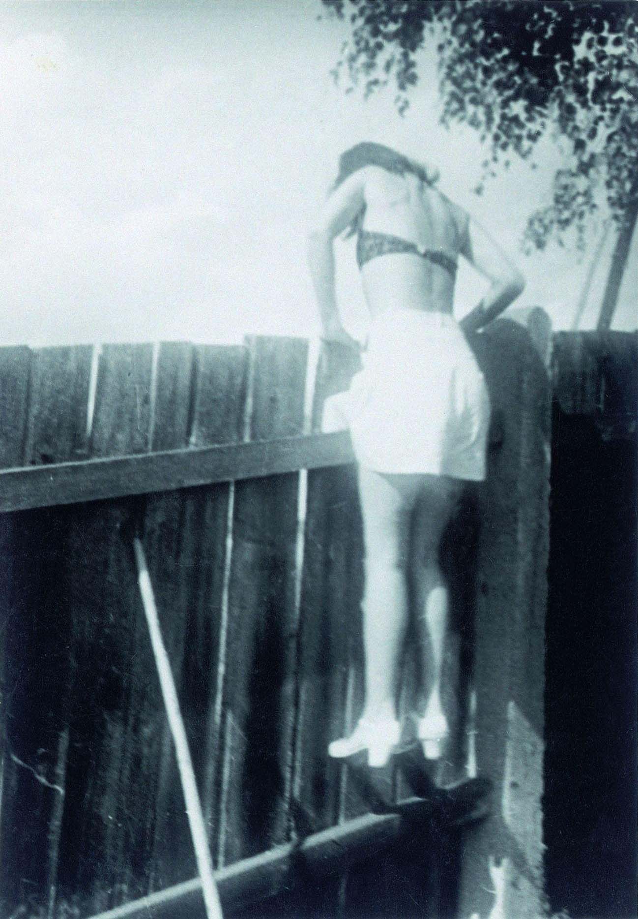 Girl in a short skirt and bikini top climbing over a wooden fence, Germany, 1940.