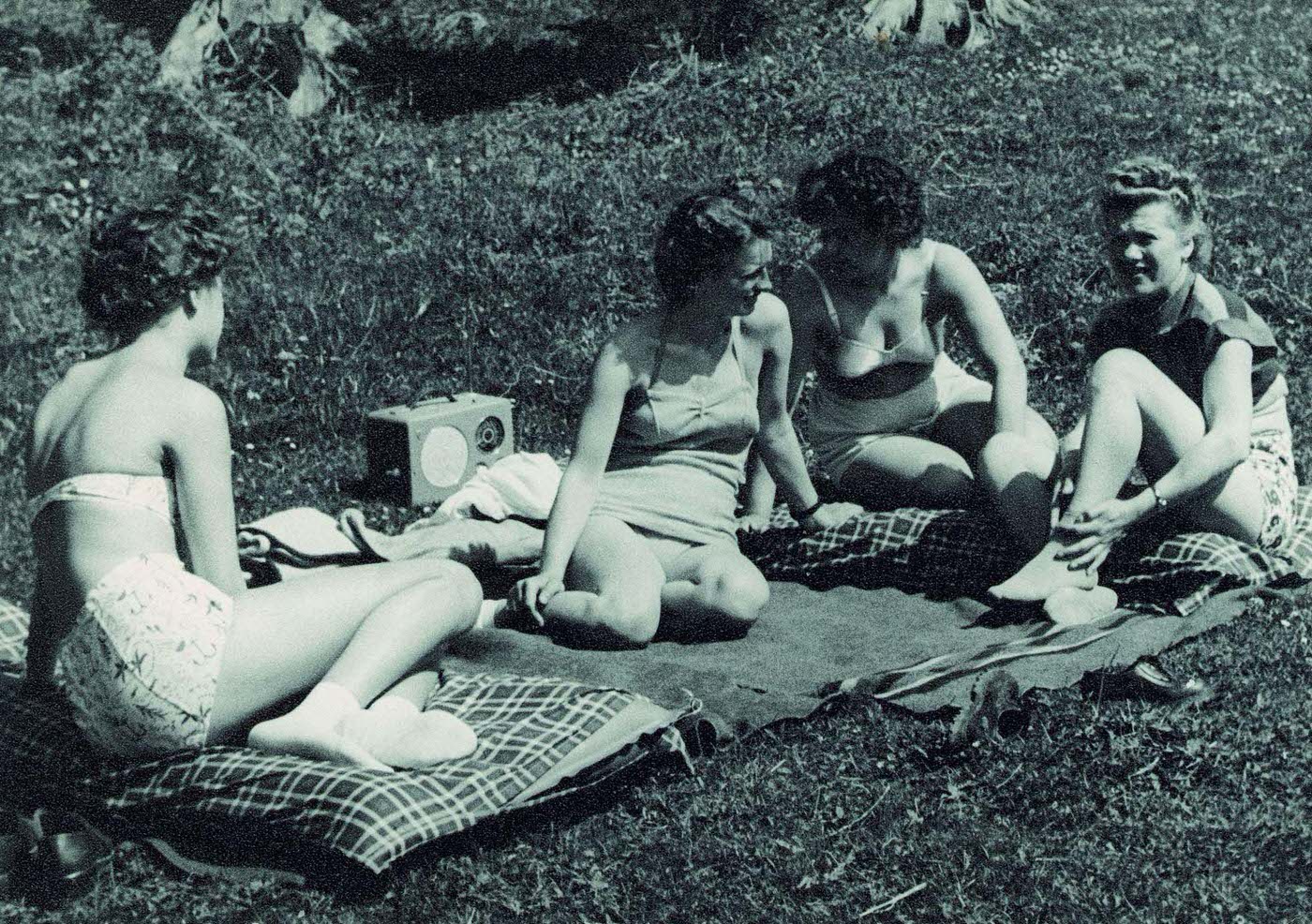 Four girls sitting on a blanket in the grass wearing swimsuits and bikinis, Switzerland, 1948.