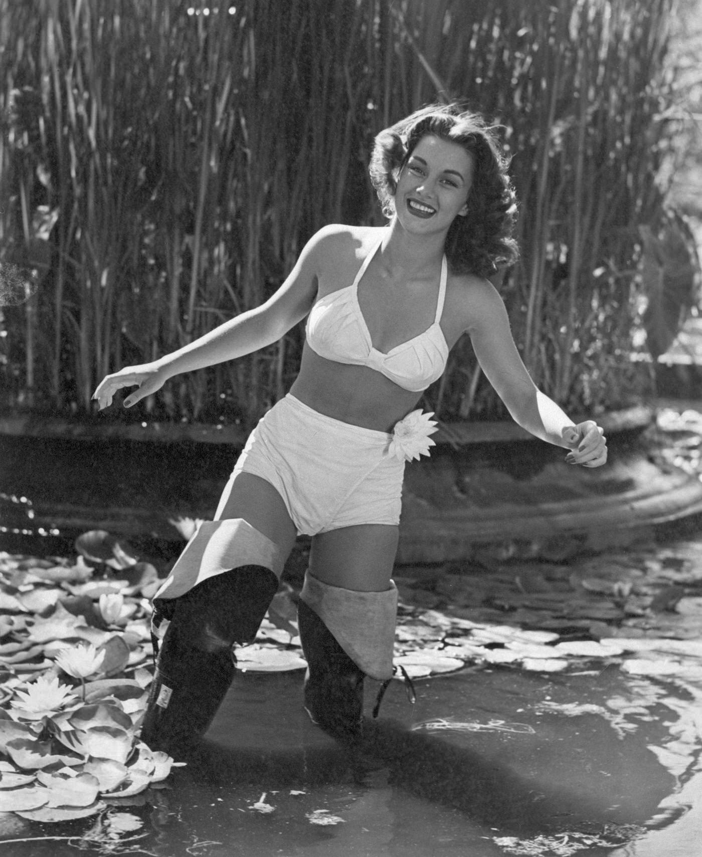 Young woman in a bikini and gumboots standing in a pond covered by water lilies, 1948.