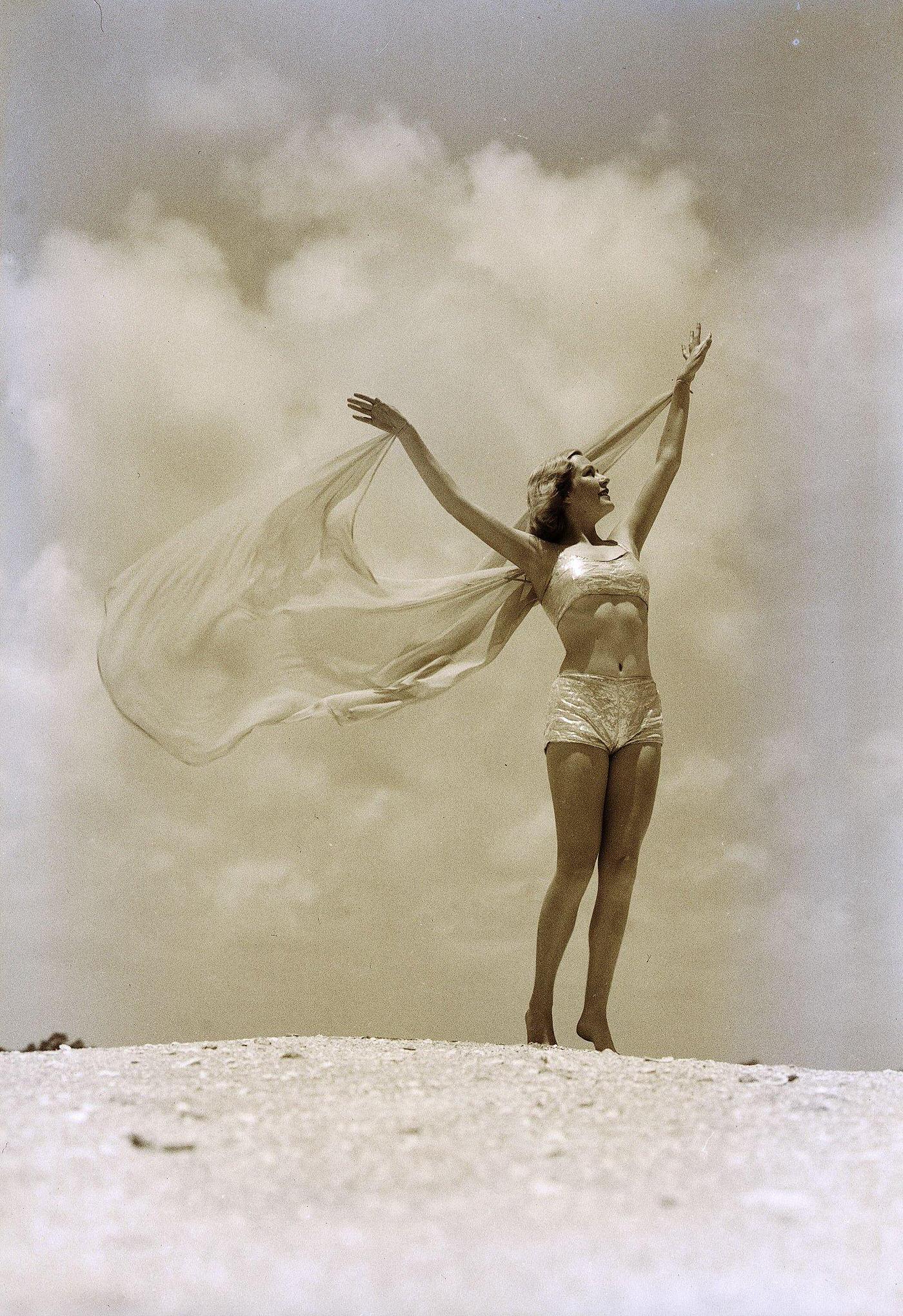 Woman in swimsuit with arms outstretched, posing on a rocky embankment