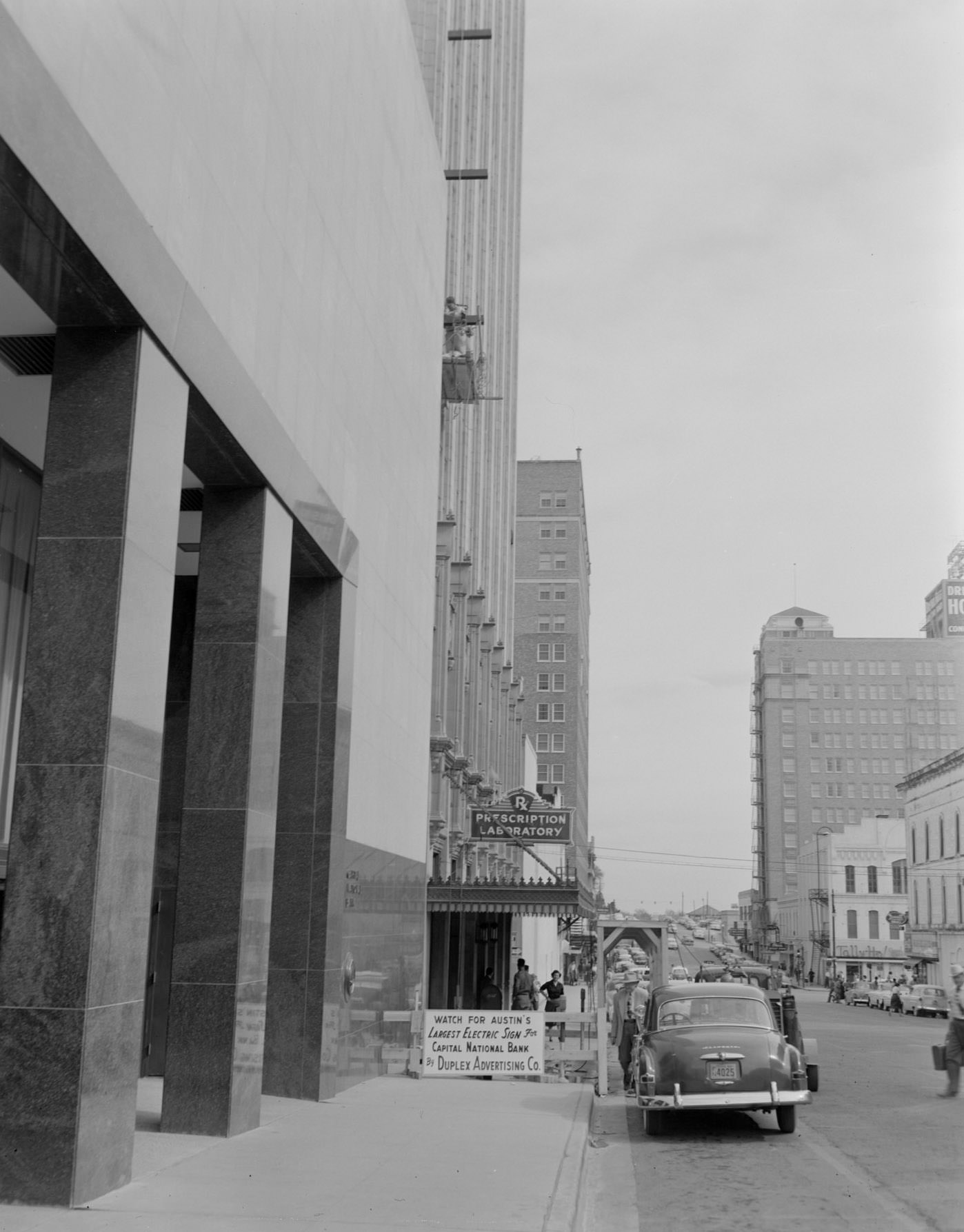 Busy Street Flanked by Large Buildings Including a Pharmacy, 1950s.