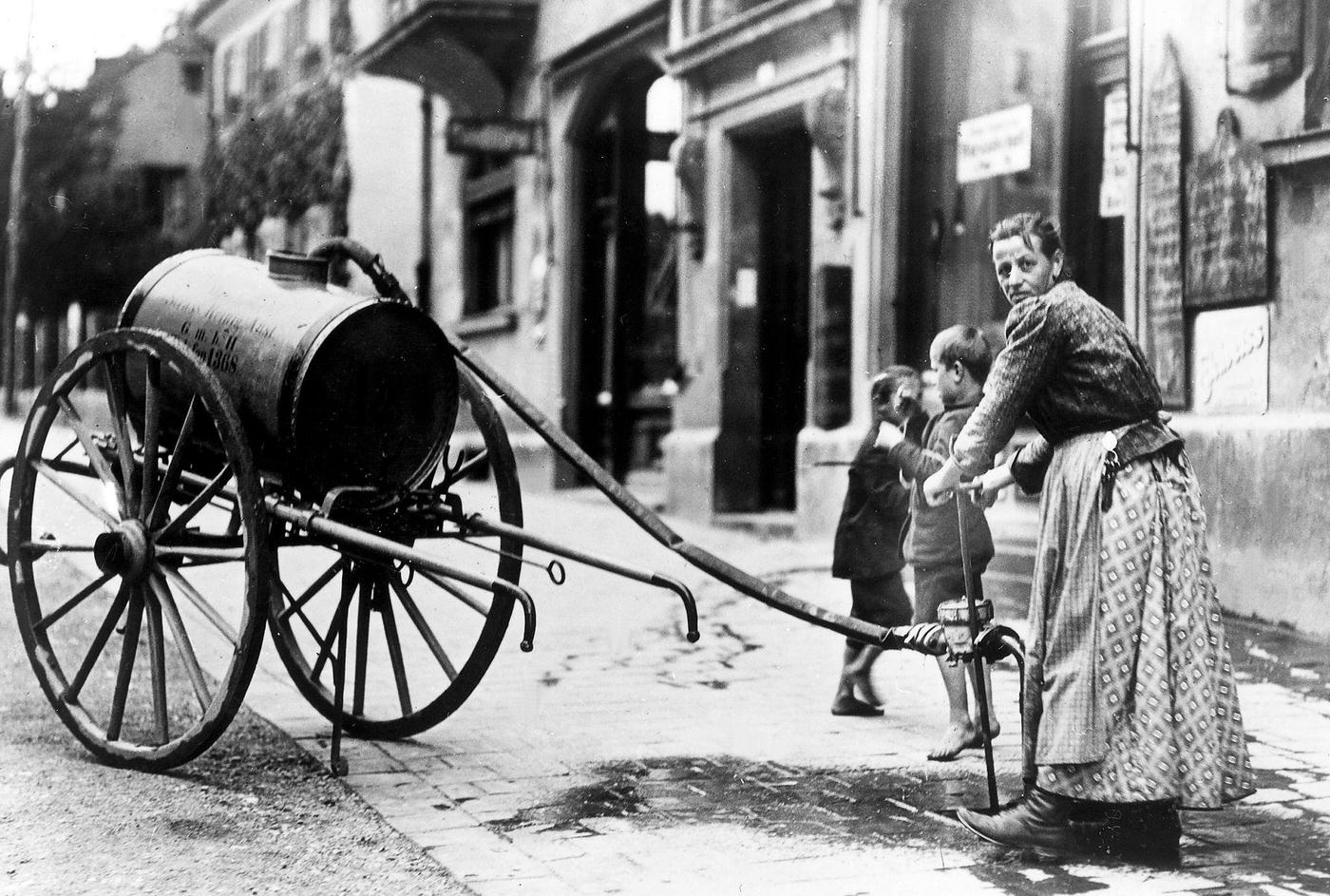 Woman refilling water container, Munich, Germany, around 1900.