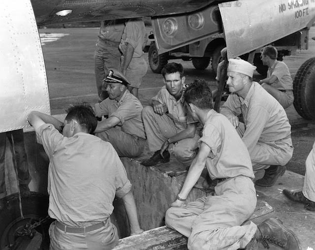 Manhattan Project scientists and military personnel gather around the bomb pit, ready to watch the Little Boy bomb being loaded into the Enola Gay.