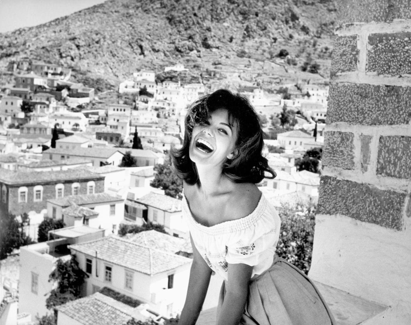 Giorgia Moll laughing on a balcony, filming 'Island of Love,' Greece, 1962