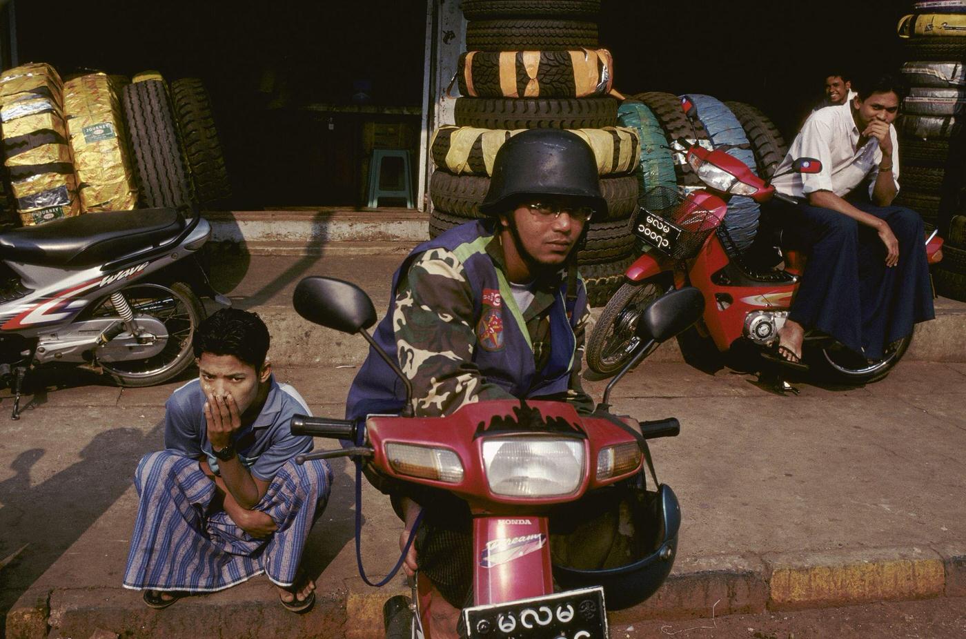 Myanmar - Man on a Motorcycle Wearing Copy of SS German Helmet at Moulmein, 1980s