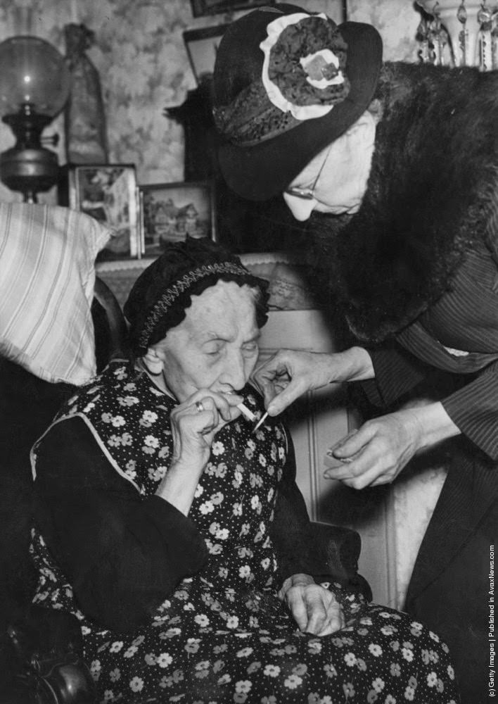 75 year-old Mary Parish lights a cigarette for her 101 year-old mother, Mary Ann Parish, at their home in Walworth, London, 14th February 1946.