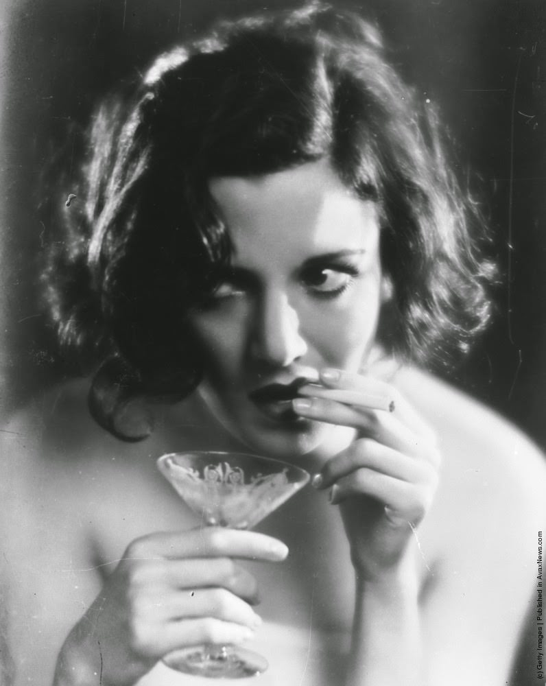 A woman smokes a cigarette while holding a cocktail glass in the other hand, 1930
